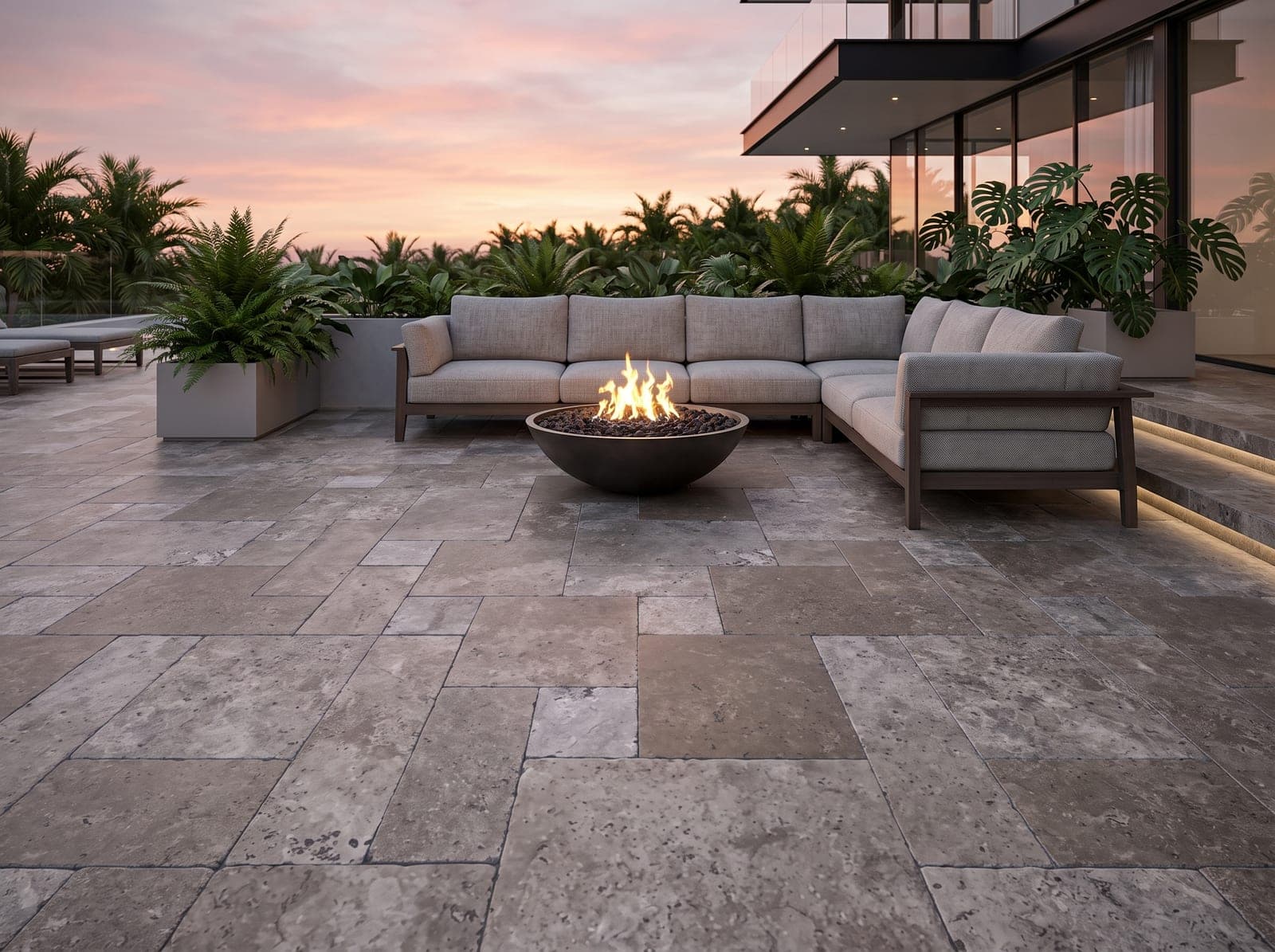 Buitenlounge in avondlicht met getrommelde Titanium cross-cut travertin, loungebank en vuurschaal